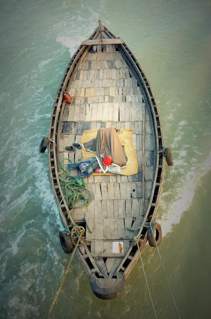 High-angle view of a wooden boat on the river in Khulna, Bangladesh, with ropes and a person resting.